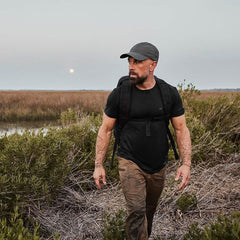 Man with GORUCK rucksack trekking through muddy wilderness at sunset