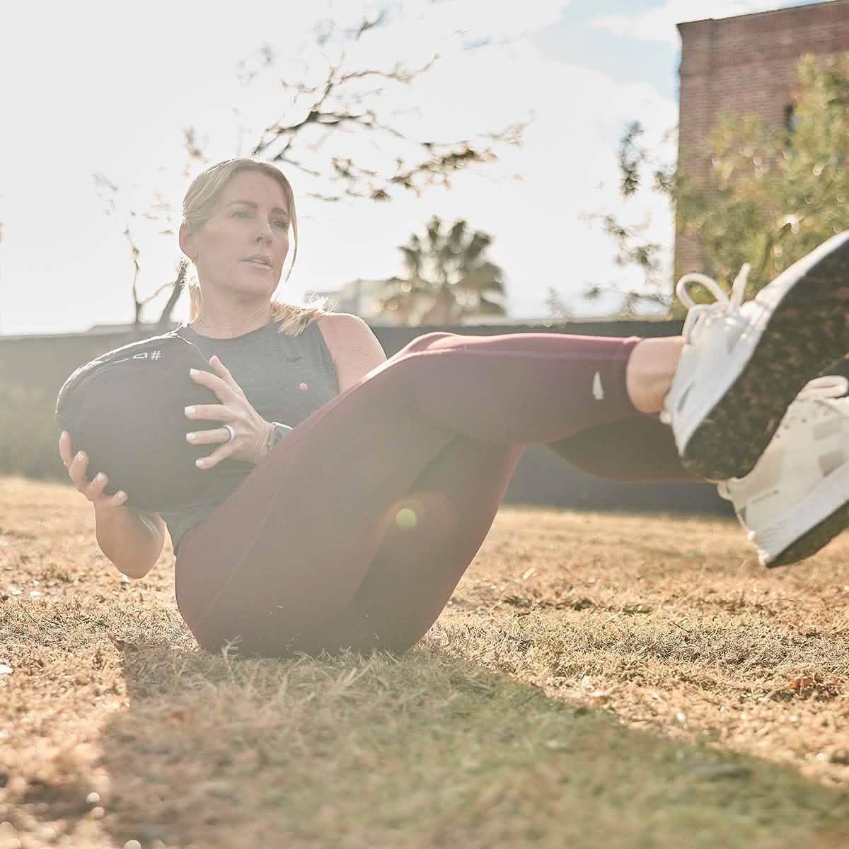 Woman outdoors using GORUCK exercise gear, performing core workout on grass in sunlight