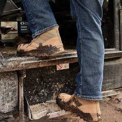 Person wearing tan GORUCK rucking boots with mud, stepping onto a truck in rugged outdoor setting