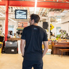 A man stands in an office, facing away, with a “DFQ” sign visible in the background.