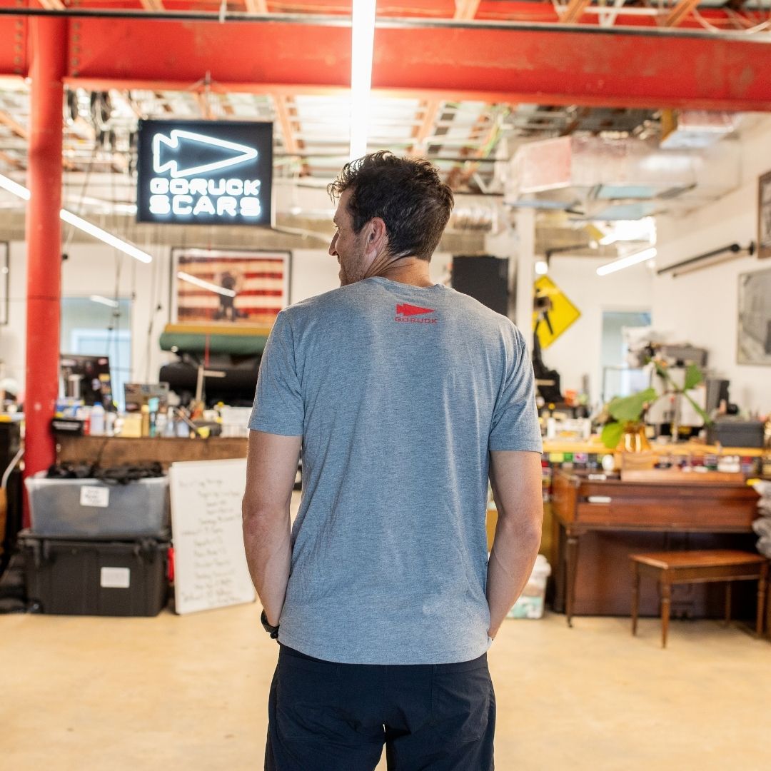 A man wearing the Graphic T-Shirt - 100% American stands with his back to the camera in a cluttered workshop space.