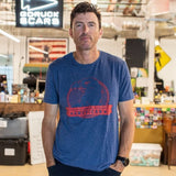 A man wearing the Graphic T-Shirt - 100% American stands in a casual, colorful office space with a “GORUCK SCARS” sign behind him.
