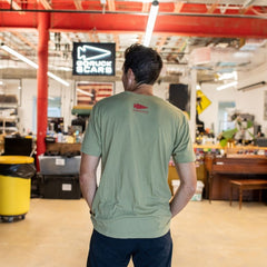 Wearing an AmeRUCKa green t-shirt, a person stands in a spacious, well-lit workshop with their back to the camera.