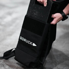 Hand placing a 45LB GORUCK ruck plate into black GORUCK backpack on concrete floor