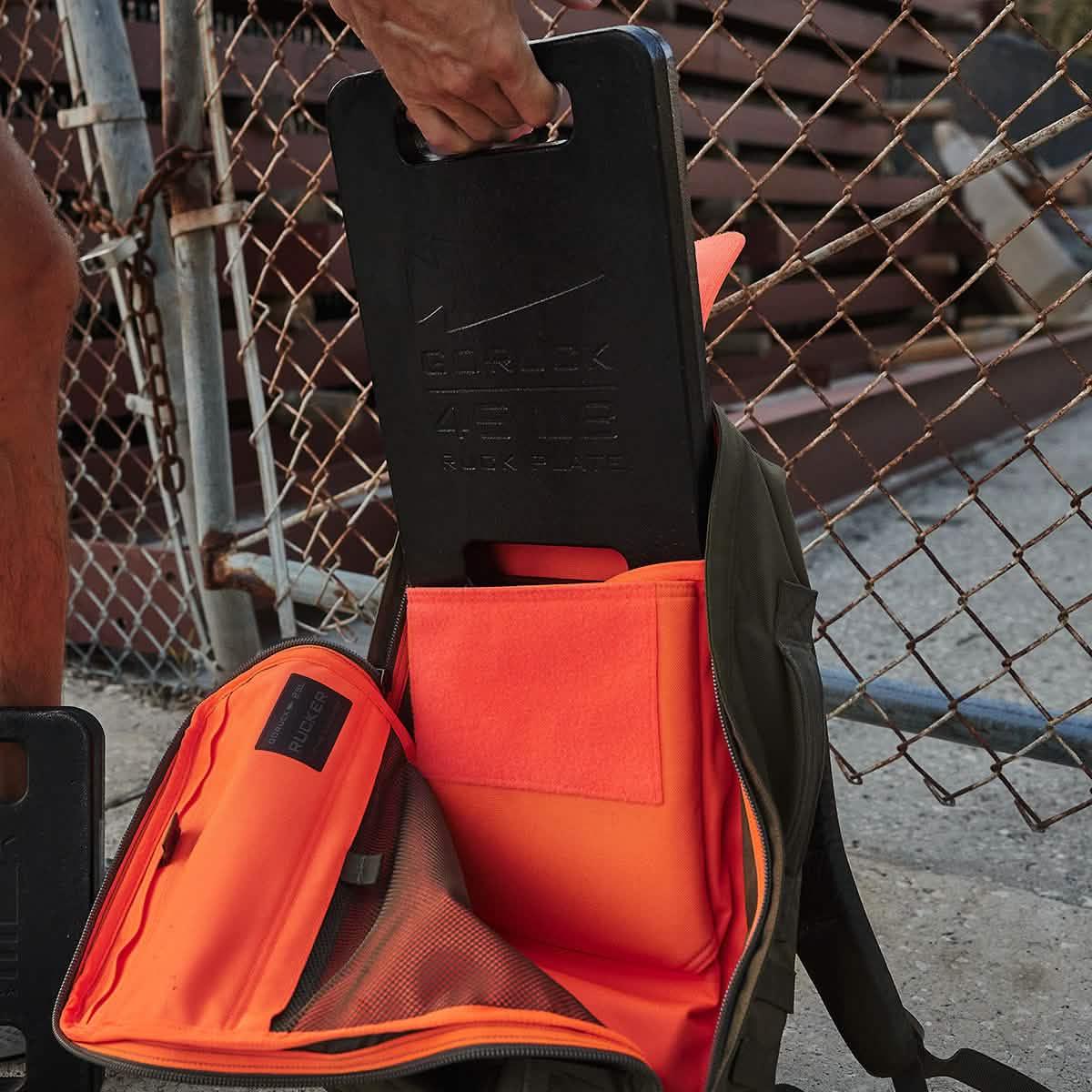 GORUCK rucksack with orange interior and ruck plate near chain-link fence