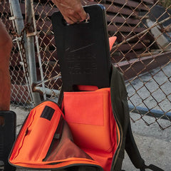 GORUCK rucksack with orange interior and ruck plate near chain-link fence