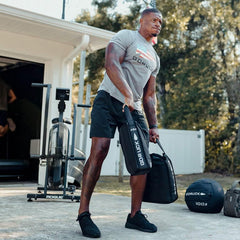 Man lifting GORUCK training sandbags outdoors, wearing GORUCK shirt and athletic gear