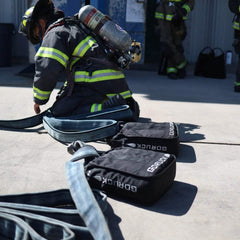 Firefighter in gear next to GORUCK rucking bags and fire hoses outdoors
