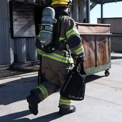 Firefighter carrying GORUCK rucking gear near a dumpster outdoors