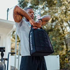 Man exercising outdoors with GORUCK weighted training bag, American flag in background