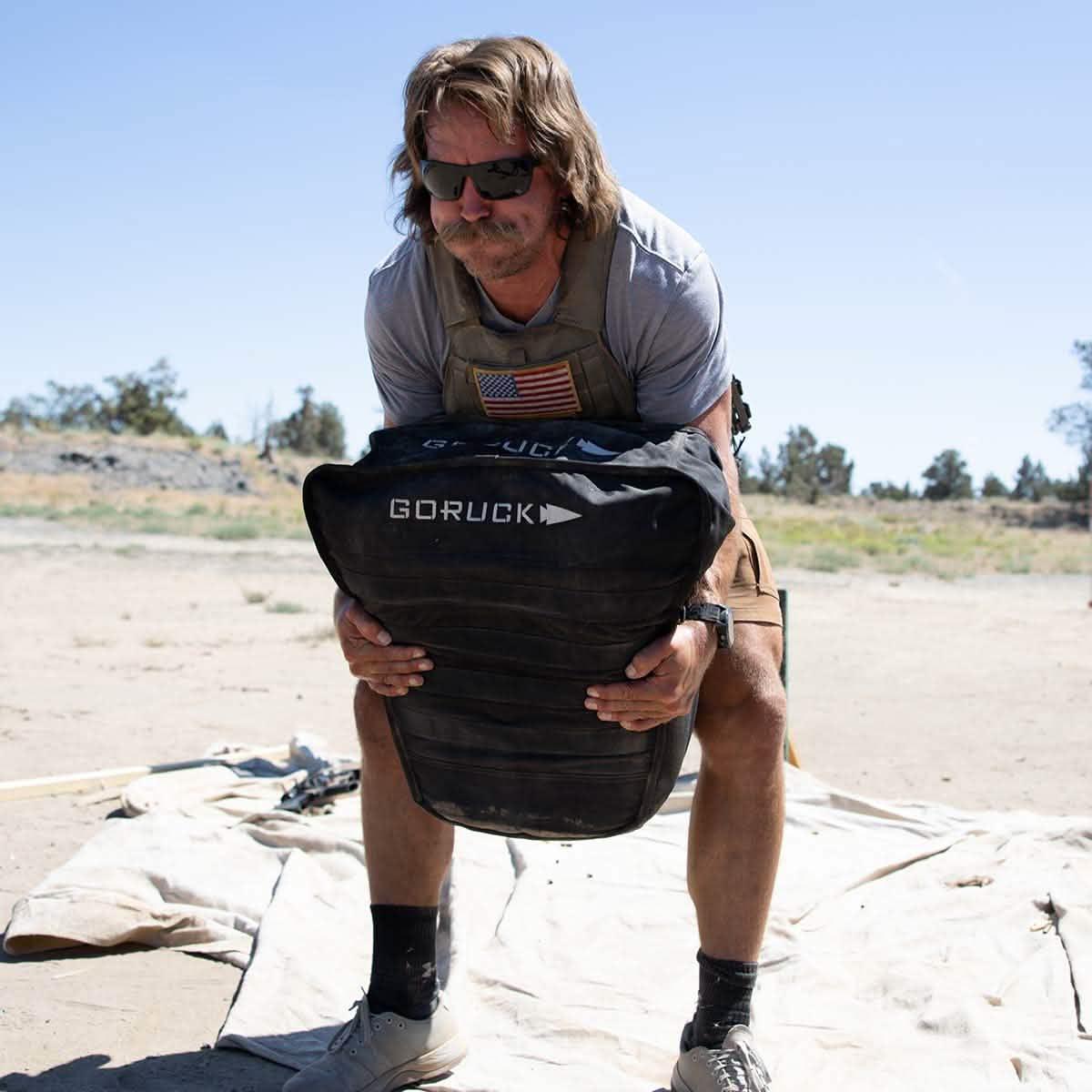 Man lifting GORUCK rucking sandbag outdoors during GORUCK event fitness training