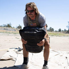 Man lifting GORUCK rucking sandbag outdoors during GORUCK event fitness training
