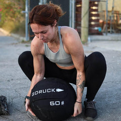 Woman lifting GORUCK 60 pound ruck sandbag outdoors during functional fitness training.