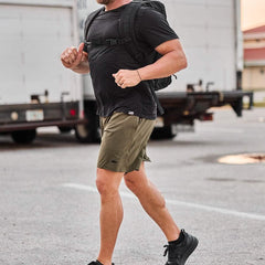 Man rucking outdoors in GORUCK gear, wearing olive shorts, black shirt, and backpack