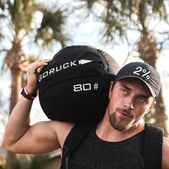 Man carrying GORUCK 80lb sandbag outdoors, showcasing rucking fitness gear.