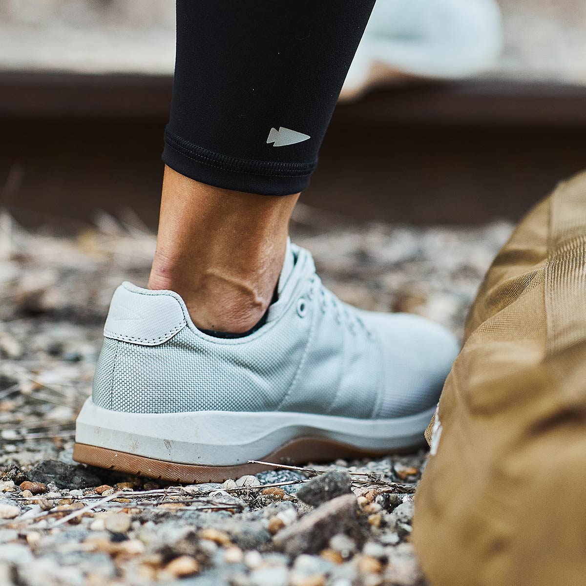 Close-up of a person wearing light gray sneakers and black leggings standing on gravel.