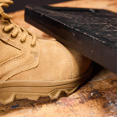 GORUCK tan rucking boot demonstrating durability under heavy black weight on wooden surface