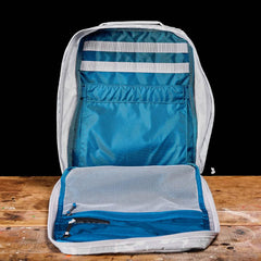 Open GR0 - Ripstop ROBIC® compact rucksack in gray and blue on a wooden surface, revealing multiple compartments and mesh pockets inside—ideal for minimalist everyday carry.