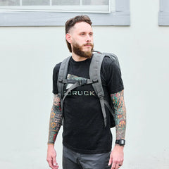 Man wearing GORUCK t-shirt and grey rucksack, showcasing rugged rucking gear outdoors.