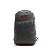 The Double Compartment Bullet Ruck - Heritage Waxed Canvas - 18L is a gray backpack with a brown leather patch and bottom, plus a diagonal front zipper pocket—ideal as a stylish travel daypack.