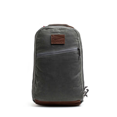 The Double Compartment Bullet Ruck - Heritage Waxed Canvas - 18L is a gray backpack with a brown leather patch and bottom, plus a diagonal front zipper pocket—ideal as a stylish travel daypack.
