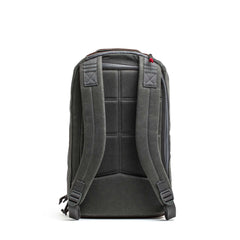 The Double Compartment Bullet Ruck - Heritage Waxed Canvas - 18L is shown from the back, featuring padded shoulder straps and a top handle.