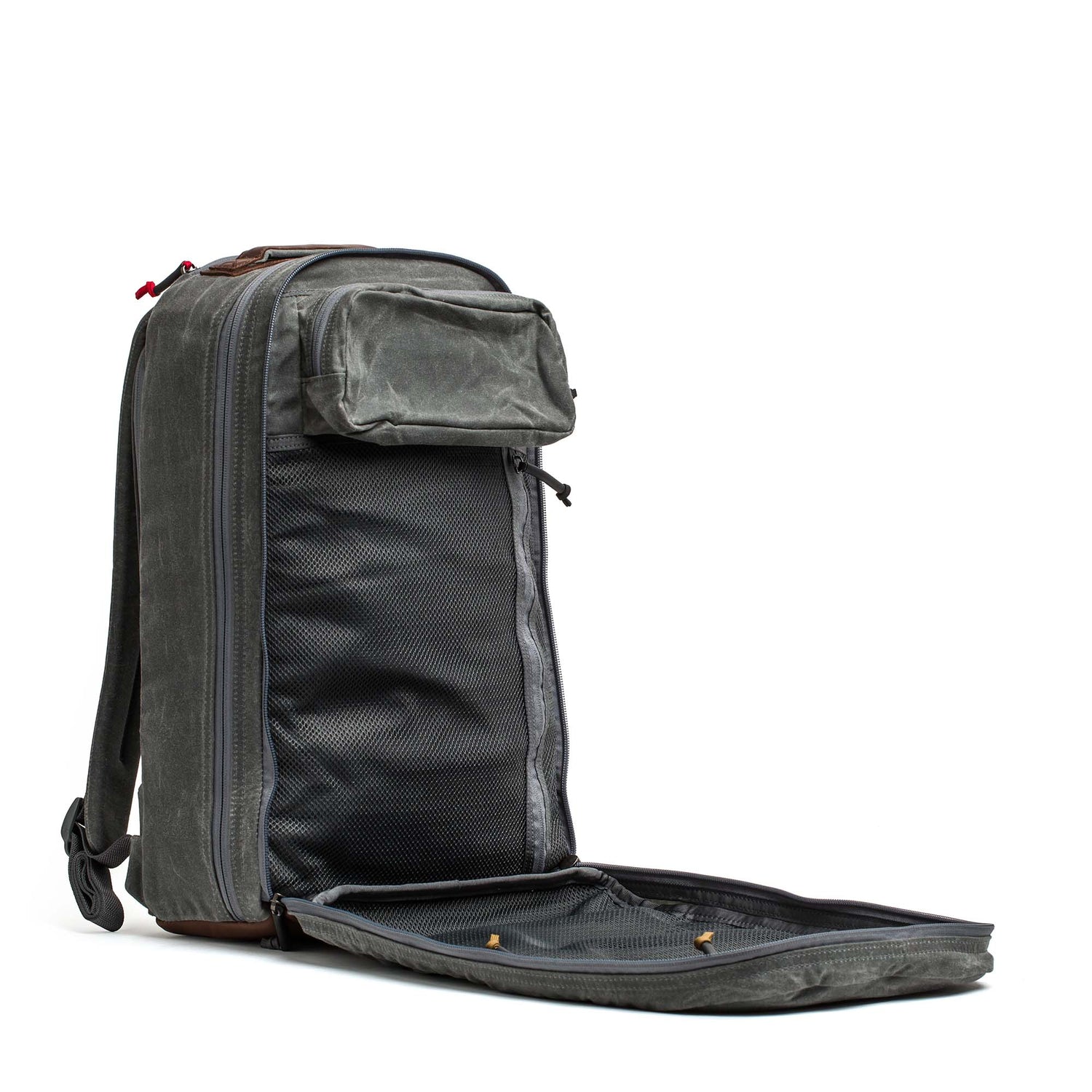 The Double Compartment Bullet Ruck - Heritage Waxed Canvas - 18L stands upright with its front compartment unzipped, revealing inner mesh pockets—ideal for use as a travel daypack.