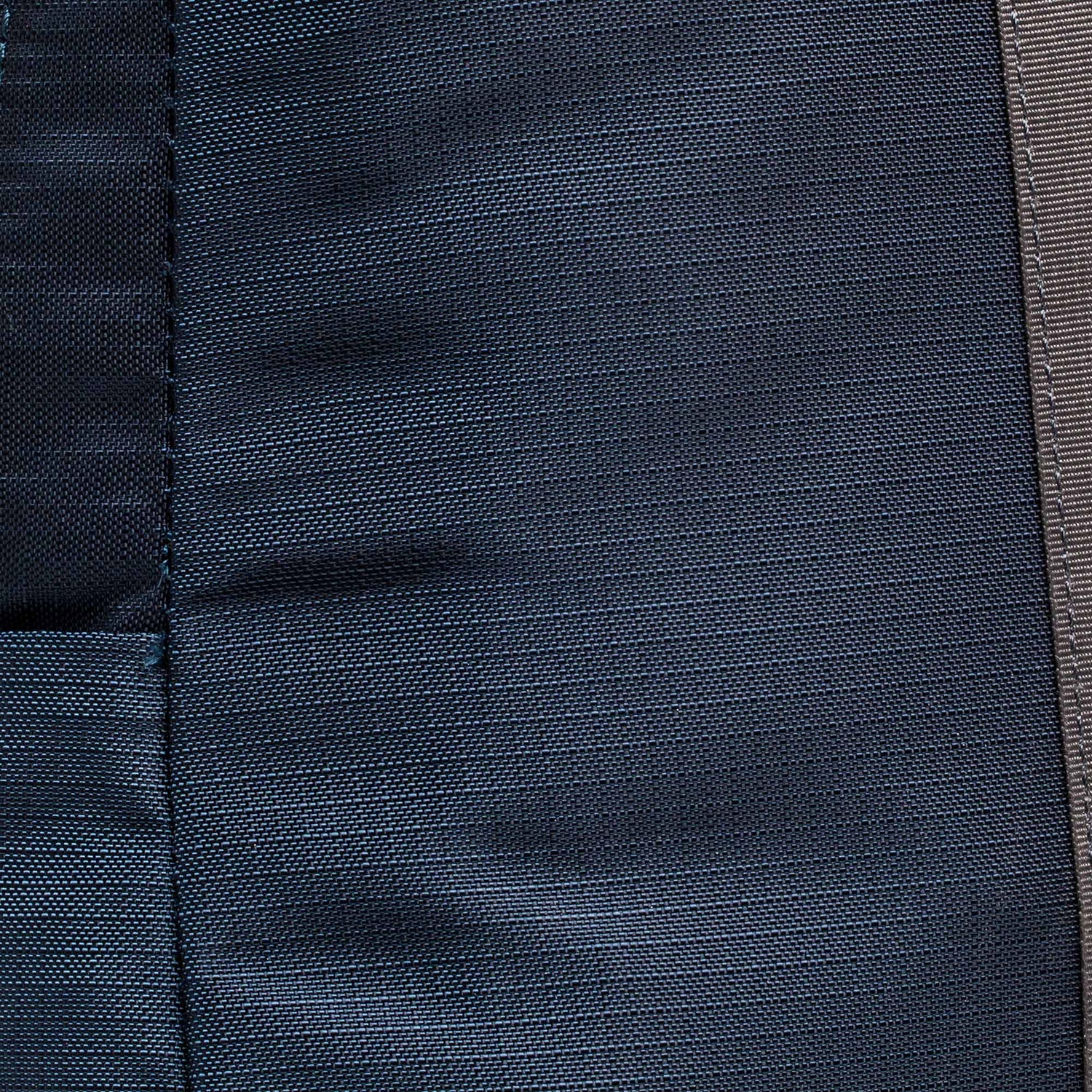 Close-up of dark blue fabric with a vertical seam and visible stitching details, similar to the rugged materials used in the Basic Rucker.