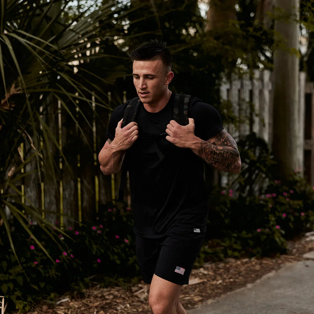 Man rucking outdoors in GORUCK gear with black shirt and backpack, American flag patch on shorts