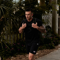 Man rucking outdoors in GORUCK gear with black shirt and backpack, American flag patch on shorts