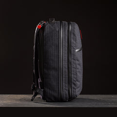 A limited-edition Bullet Ruck x Carryology - GRXC2 Samurai 2.0 backpack in black with vertical stitching, side zippers, and a red zipper pull, inspired by the JPXDP 17oz Black Samurai Sashiko, shown against a dark background.
