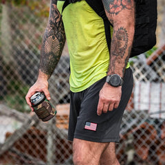 Tattooed man in GORUCK rucking gear holding a camo can, American flag patch shorts