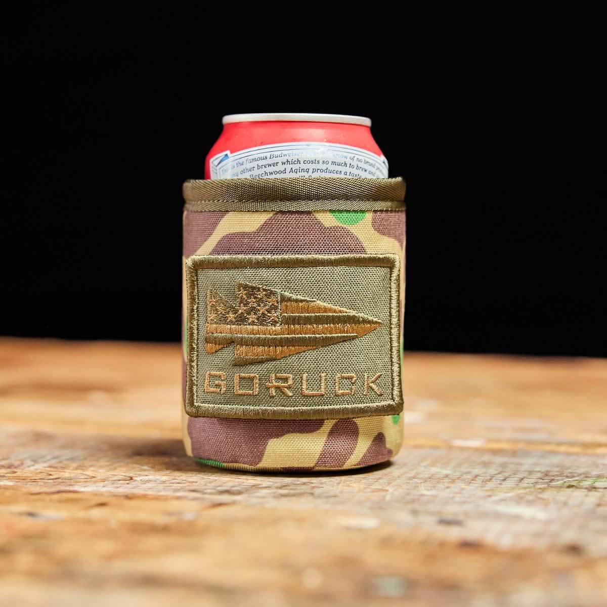 GORUCK camouflage can koozie with logo patch on wooden surface