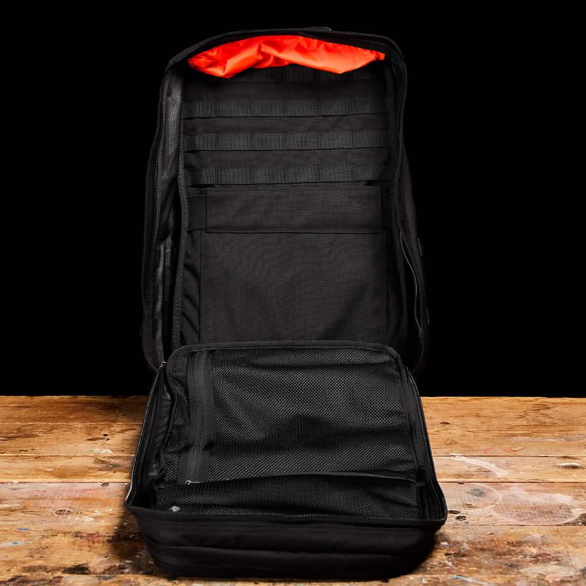 GORUCK black 40L rucksack open, showing interior mesh pockets and orange lining on wooden table
