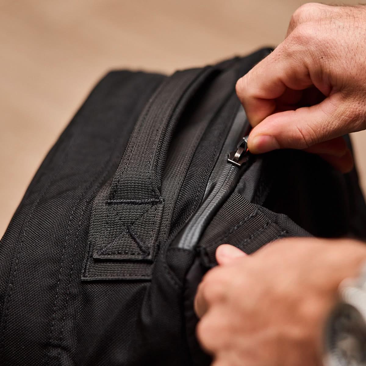 Hand zipping a rugged black GORUCK backpack, close-up of durable gear