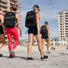 Women rucking on beach wearing GORUCK backpacks, athletic apparel, and sneakers.