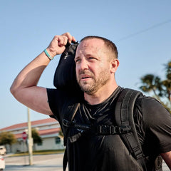 Man wearing GORUCK Tough Mesh Tee and backpack outdoors, carrying rucking gear.