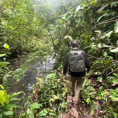 Man hiking with GORUCK backpack on jungle trail beside river