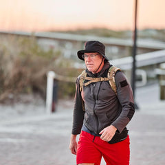 Man rucking in GORUCK gear with black boonie hat, outdoor trail background, red shorts