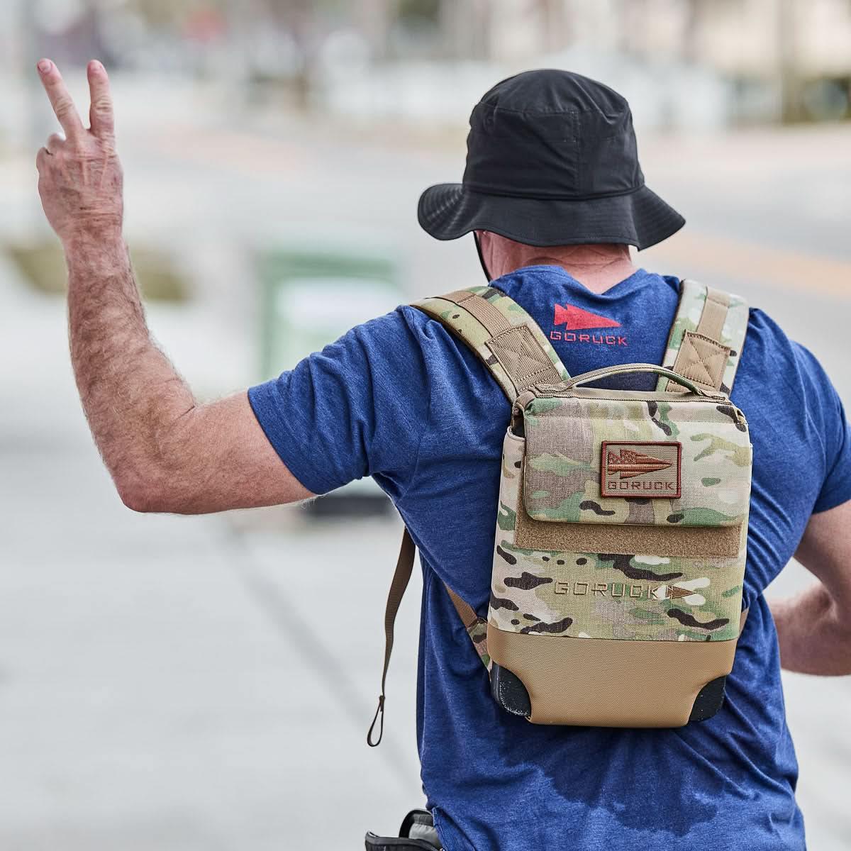 Man wearing a black boonie hat, blue GORUCK shirt, and camo GORUCK rucksack outdoors.