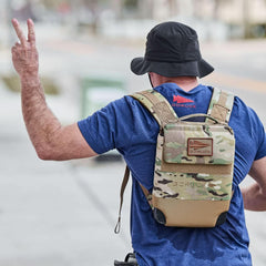 Man wearing a black boonie hat, blue GORUCK shirt, and camo GORUCK rucksack outdoors.