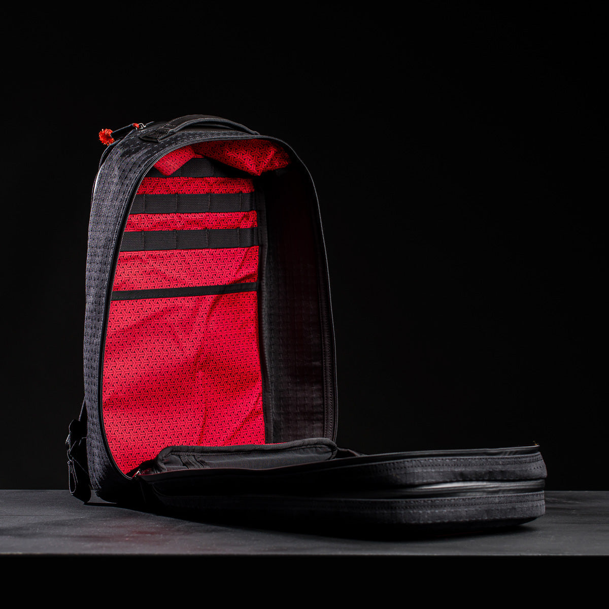 The Bullet Ruck x Carryology - GRXC2 Samurai 2.0 backpack, shown open against a dark background, reveals its bright red interior with organizational straps and pockets.