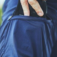 Close-up of a hand placing a black item into the zippered pocket of Men’s Challenge Shorts - Lightweight ToughDry®, blue technical shorts made with fast-drying fabric.