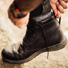 Person putting on black GORUCK rucking boot outdoors, durable hiking footwear
