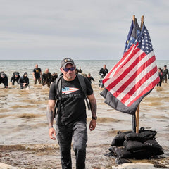 GORUCK team rucking through water with American flag on beach, rugged outdoor gear training