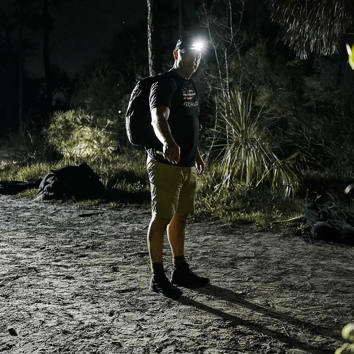 Man rucking at night wearing GORUCK Challenge Shorts, headlamp, and backpack outdoors.