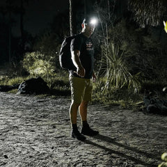 Man rucking at night wearing GORUCK Challenge Shorts, headlamp, and backpack outdoors.
