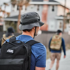 Man wearing GORUCK charcoal boonie hat and backpack, walking outdoors in urban setting