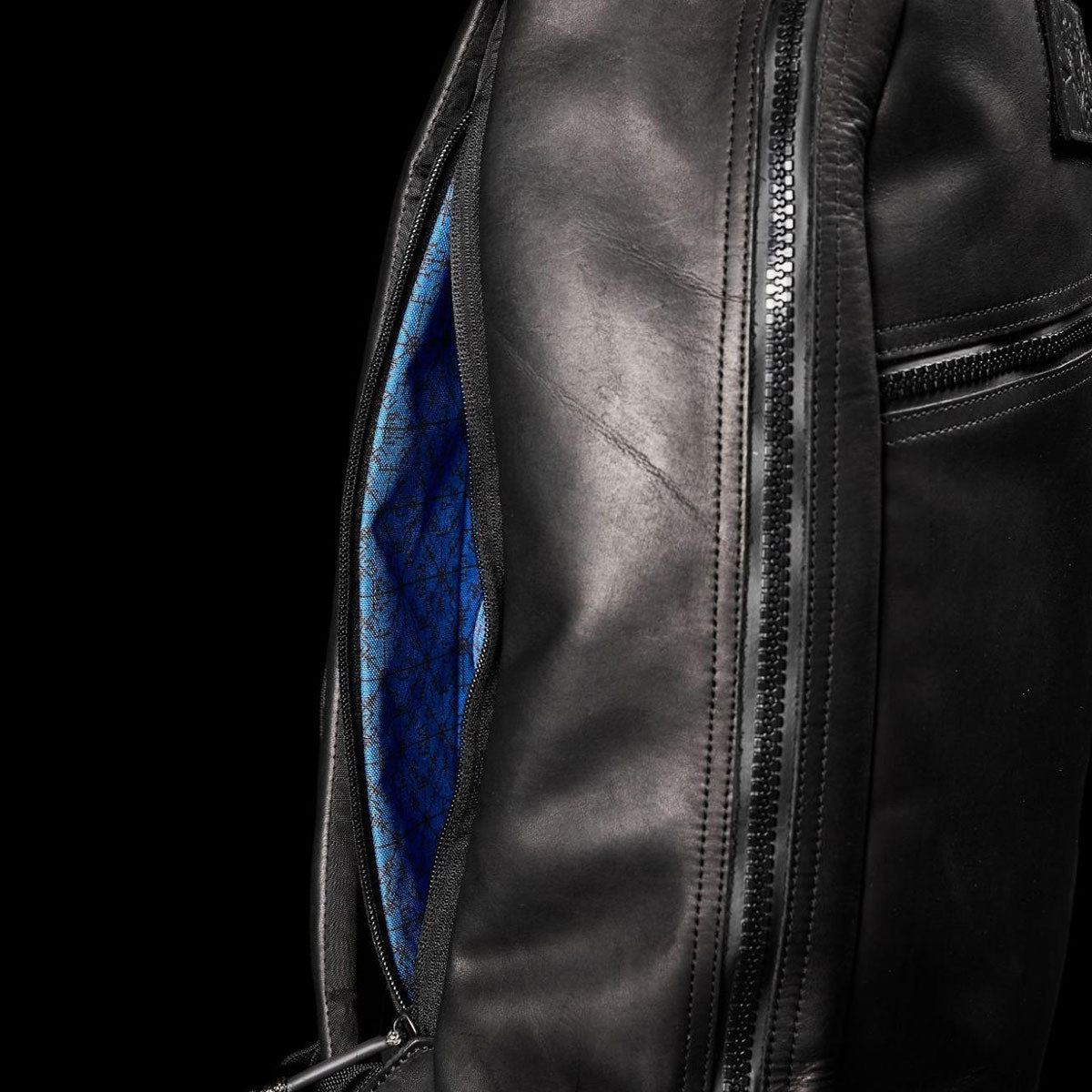 Close-up of a black leather backpack with a blue geometric-patterned inner lining, partially unzipped.