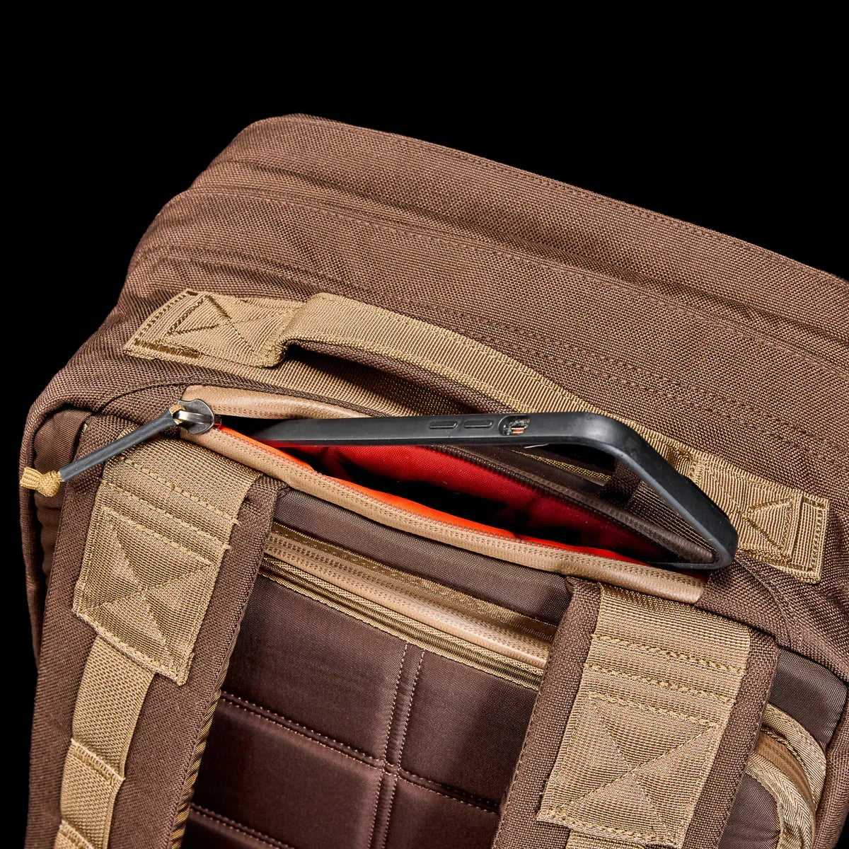 GORUCK brown rucksack with padded straps, open zipper pocket holding a smartphone